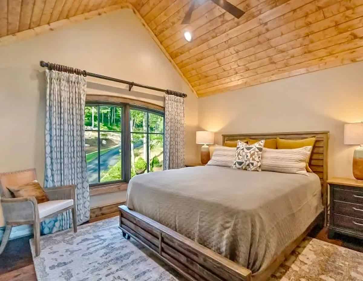 Bedroom with vaulted wood ceiling, king bed, and arched window with garden view