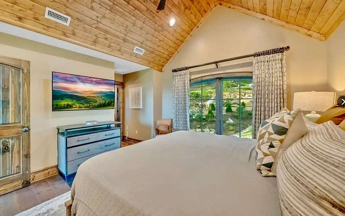 Bedroom with wood vaulted ceiling, rustic door, and mountain landscape TV