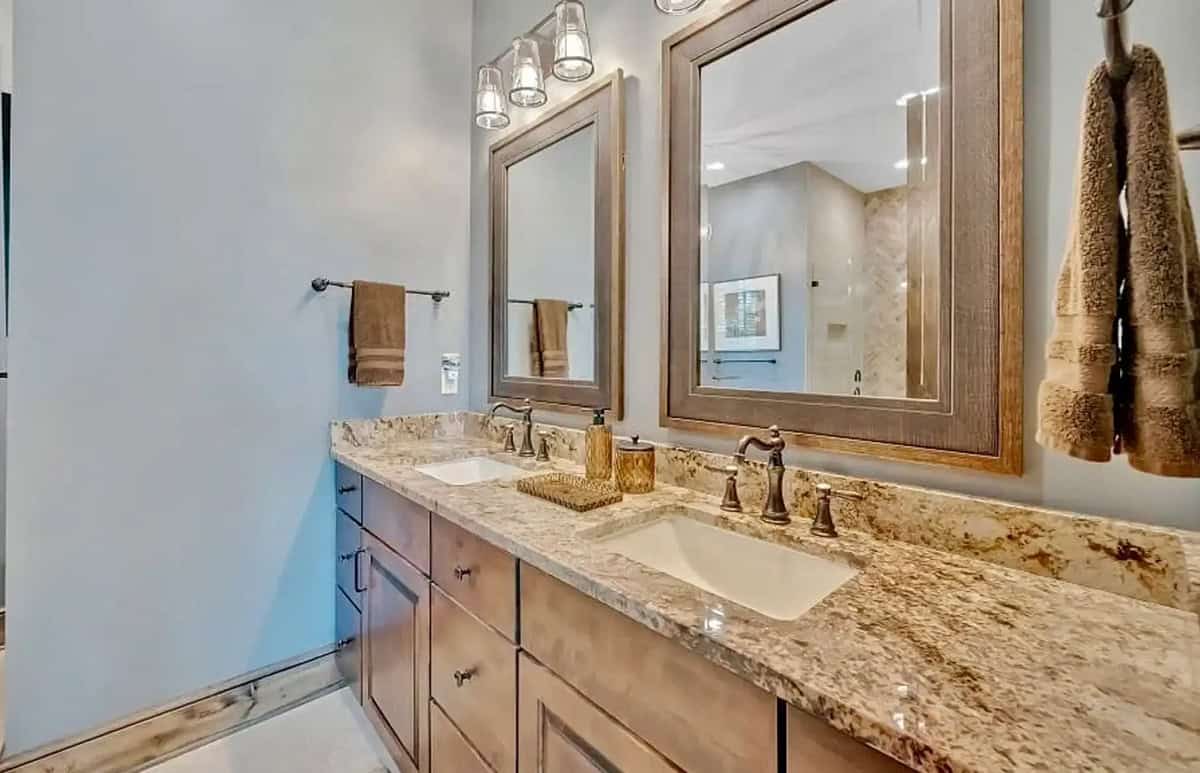 Main bath double vanity with granite countertop, wood-framed mirrors, and bronze fixtures