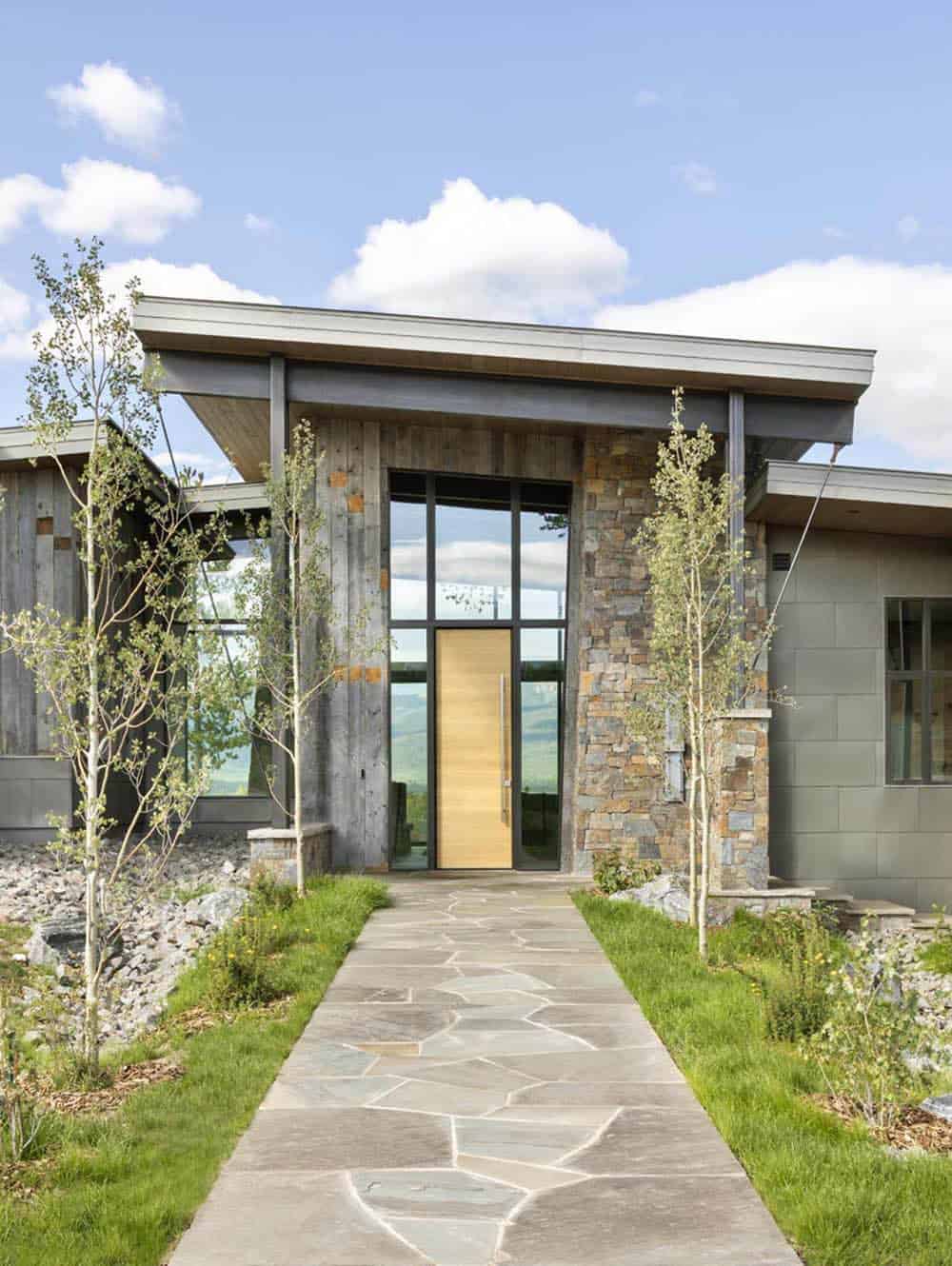 Stone and reclaimed wood entry facade with tall wood pivot door and flagstone walkway