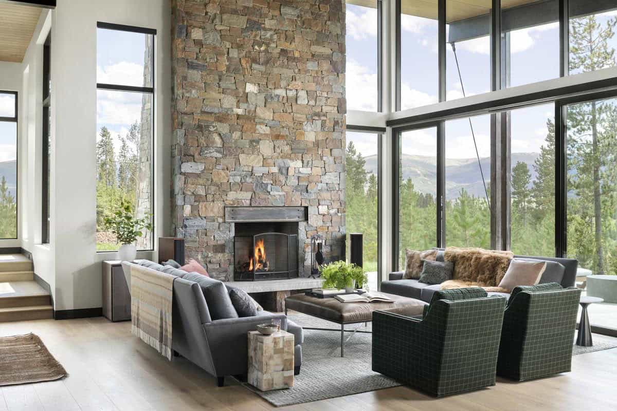 Double-height living room with stone fireplace, floor-to-ceiling windows, and mountain views