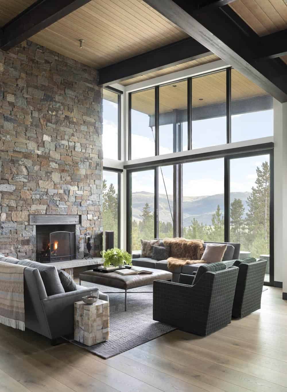 Living room with wood beam ceiling, stone fireplace, and panoramic mountain windows
