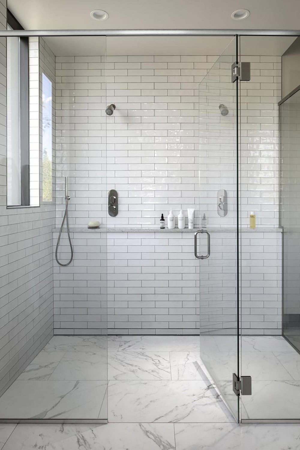 Walk-in glass shower with white subway tile walls and marble floor