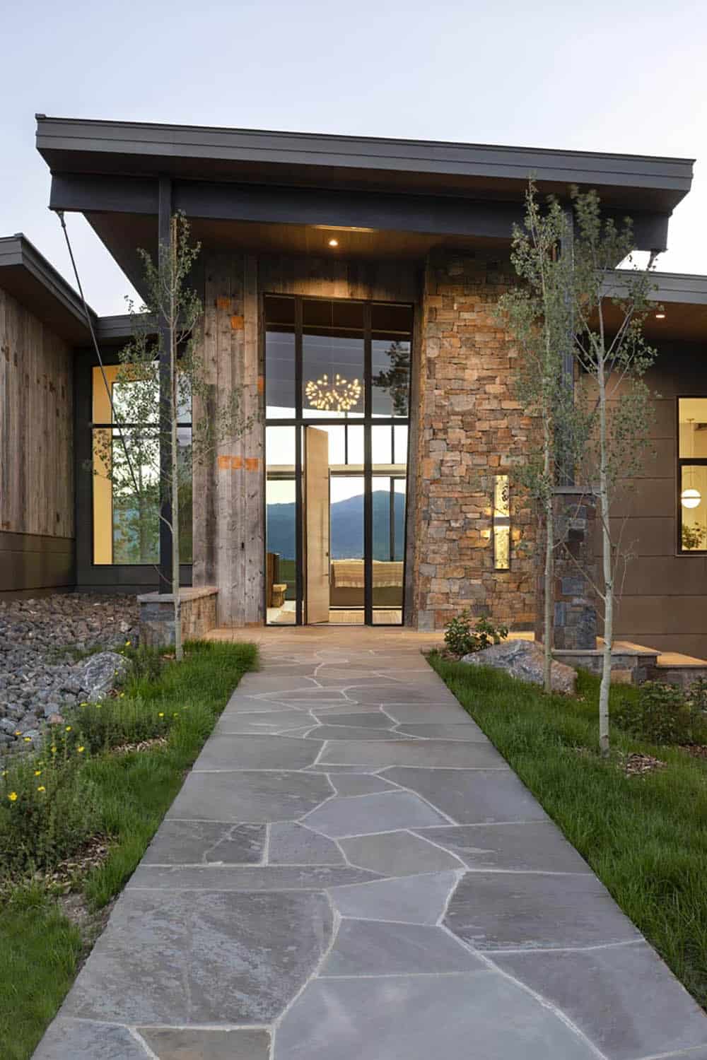 Entry facade at dusk with stone columns, glass surround, and flagstone path