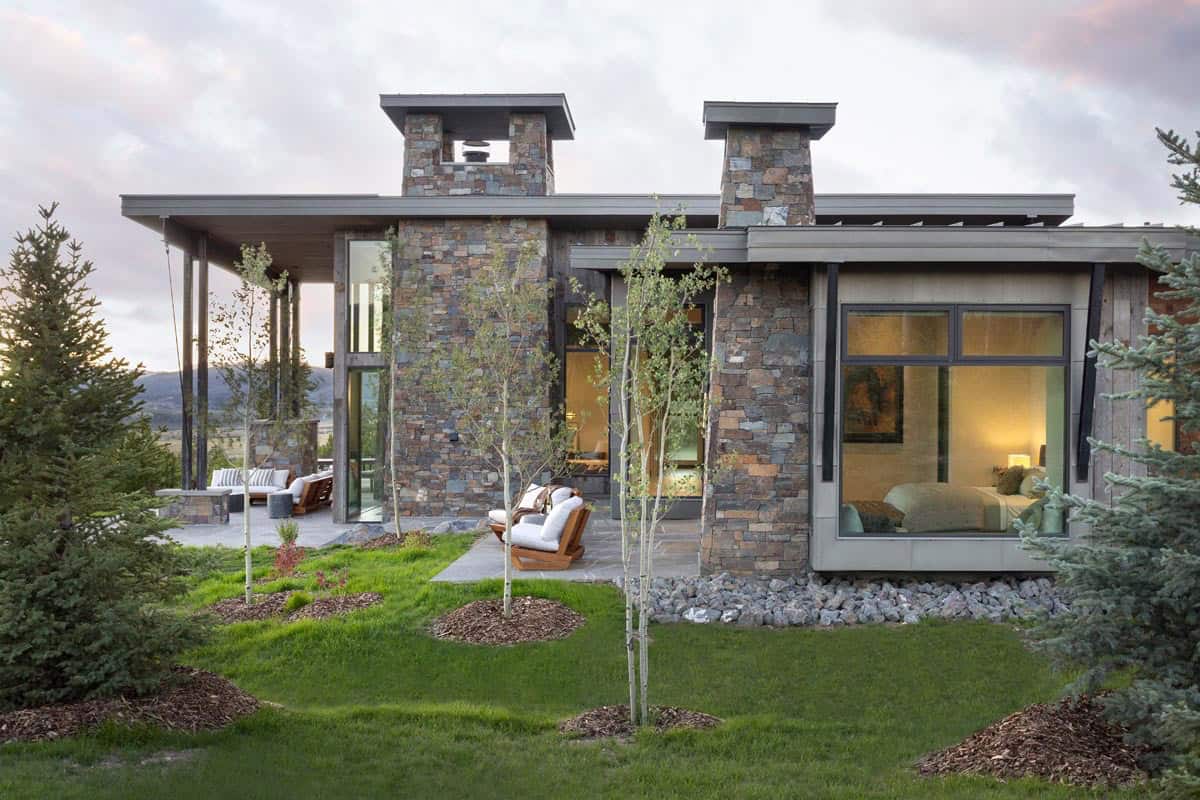 Rear exterior with stone chimneys, outdoor seating patio, and glowing bedroom windows