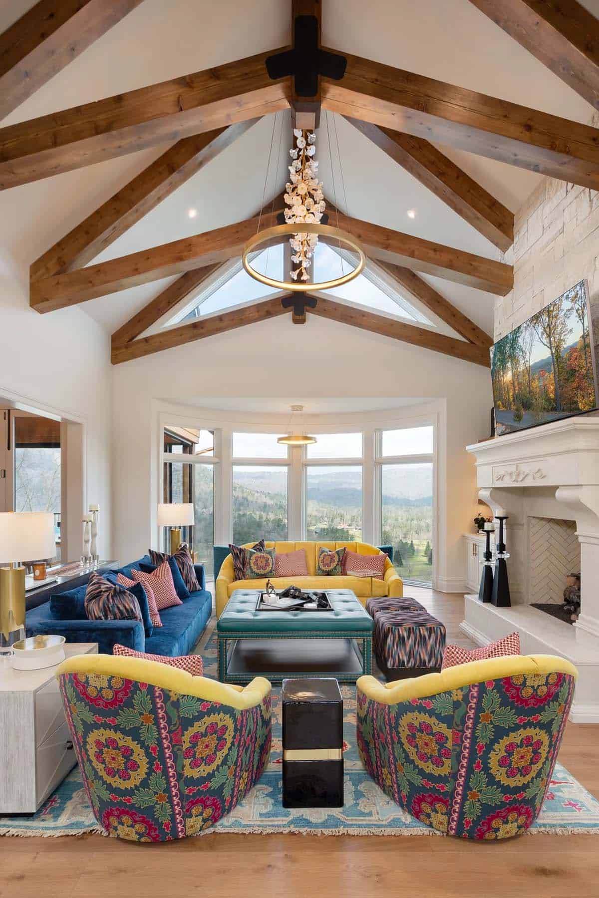 Vaulted living room with wood beams, bold patterned armchairs, blue velvet sofa, and mountain views