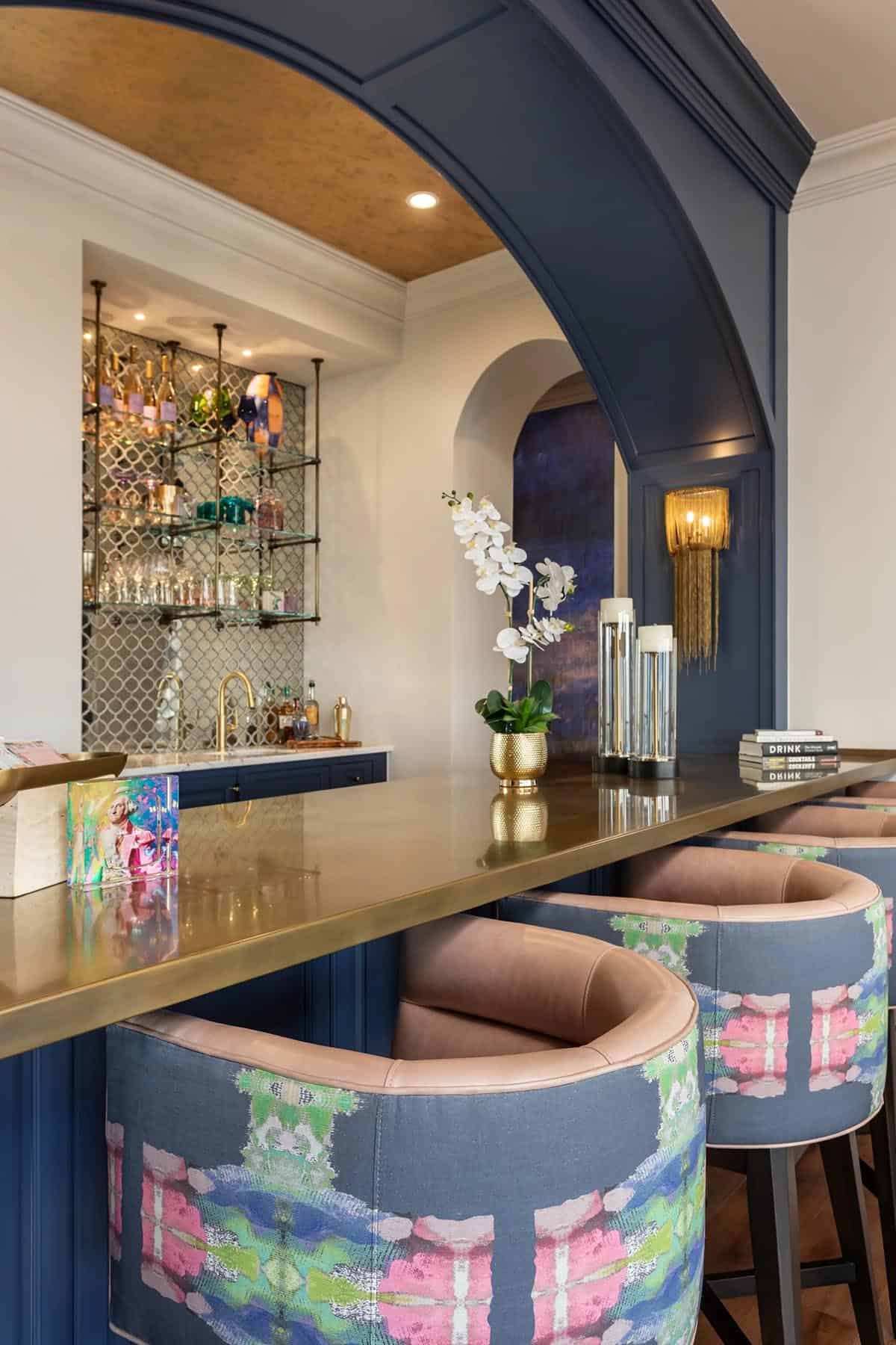 Navy and gold home bar with ikat barstools, mirrored backsplash, and arched alcove