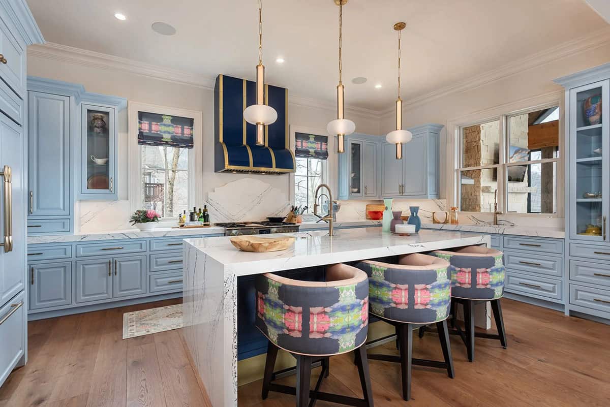 Blue kitchen with marble countertops, navy range hood with gold trim, and ikat barstools