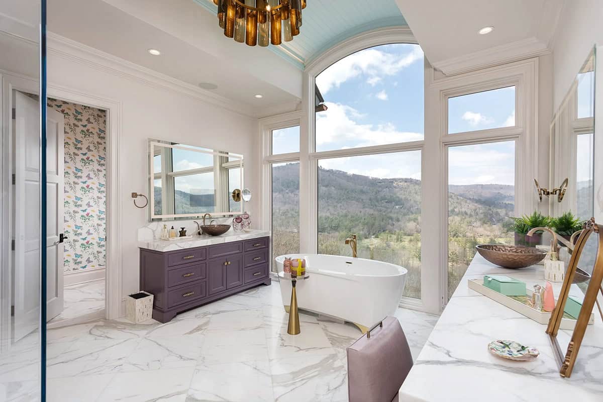 Primary bathroom with freestanding tub, purple vanities, arched windows, and mountain views