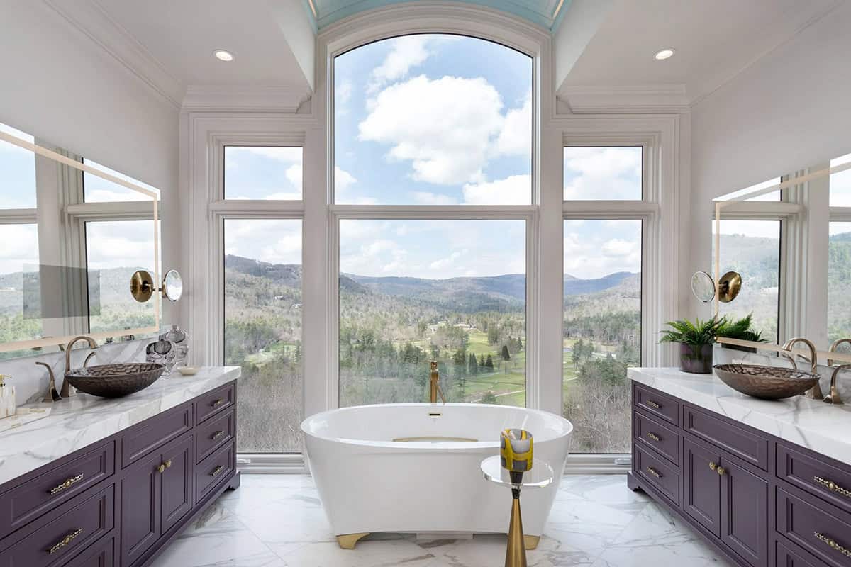 Symmetrical primary bathroom with dual purple vanities, freestanding tub, and panoramic mountain view
