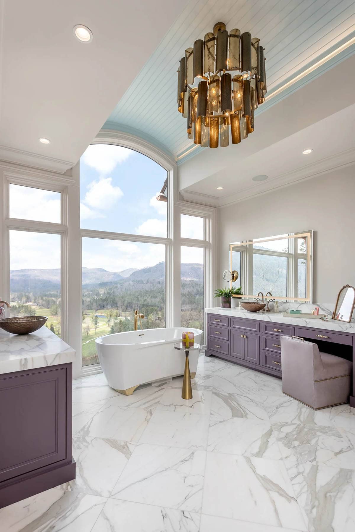 Primary bathroom with smoky gold chandelier, freestanding tub, and floor-to-ceiling mountain windows