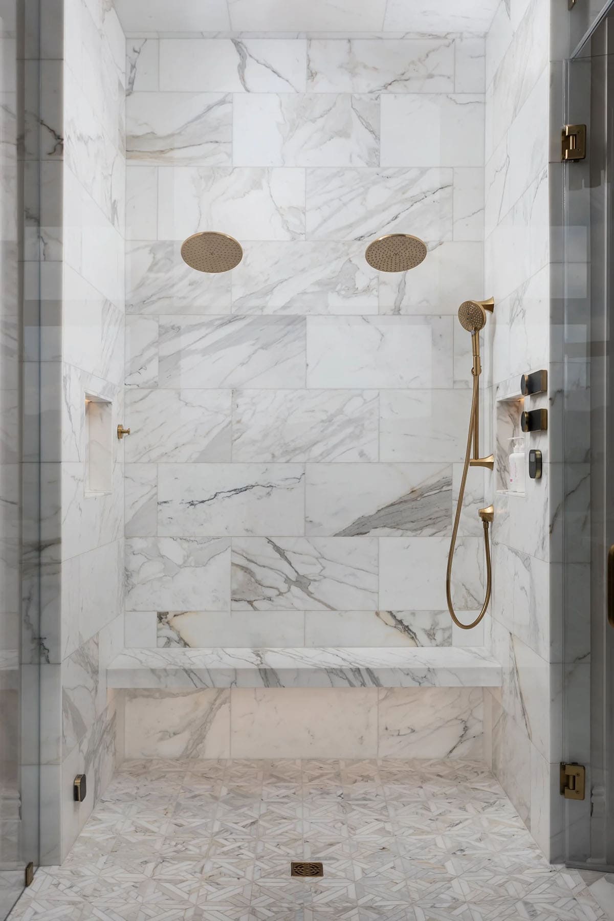All-marble shower with dual rain heads, built-in bench, and brushed gold fixtures