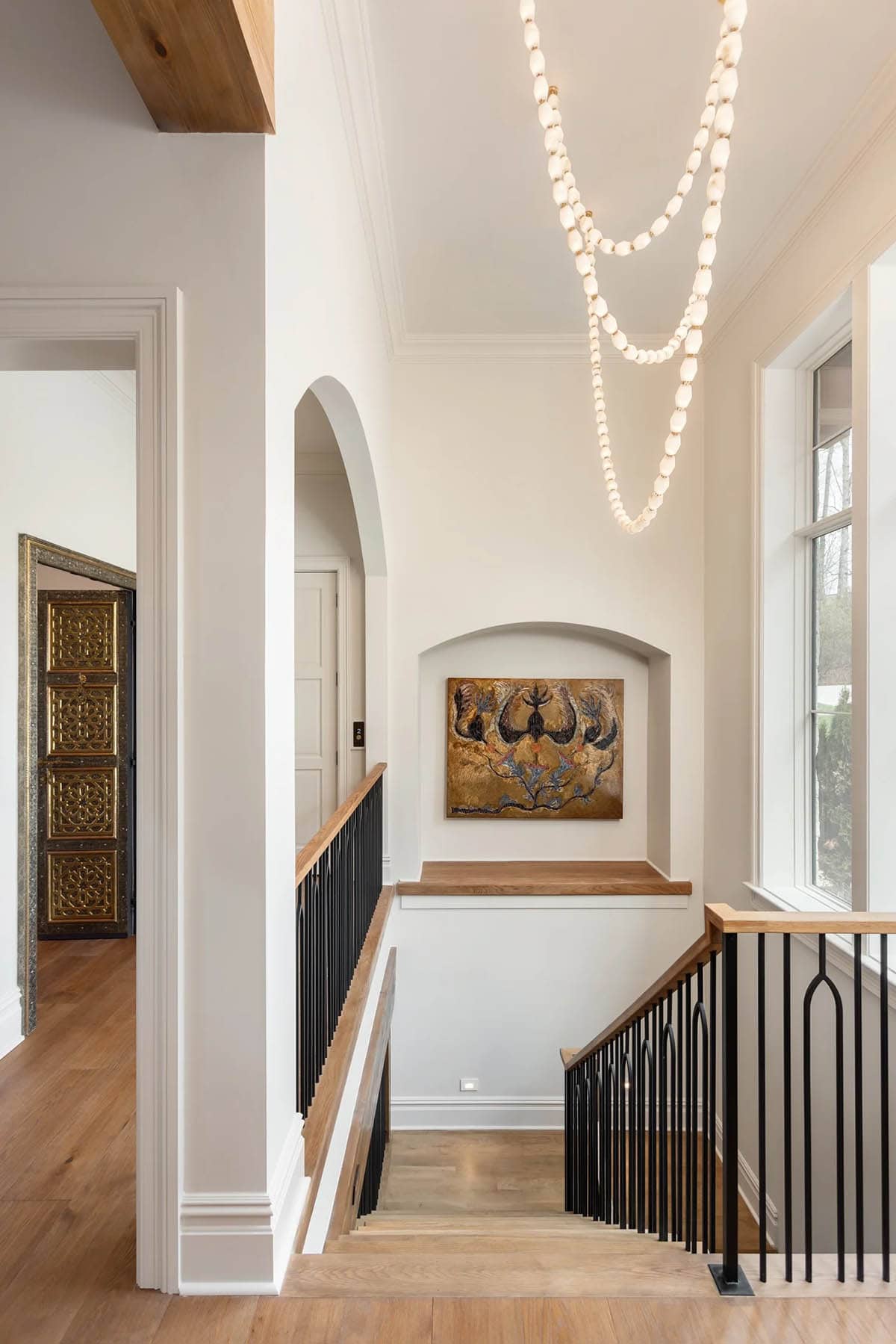 Upper hallway with beaded chandelier, art niche, oak staircase railing, and Moroccan doors