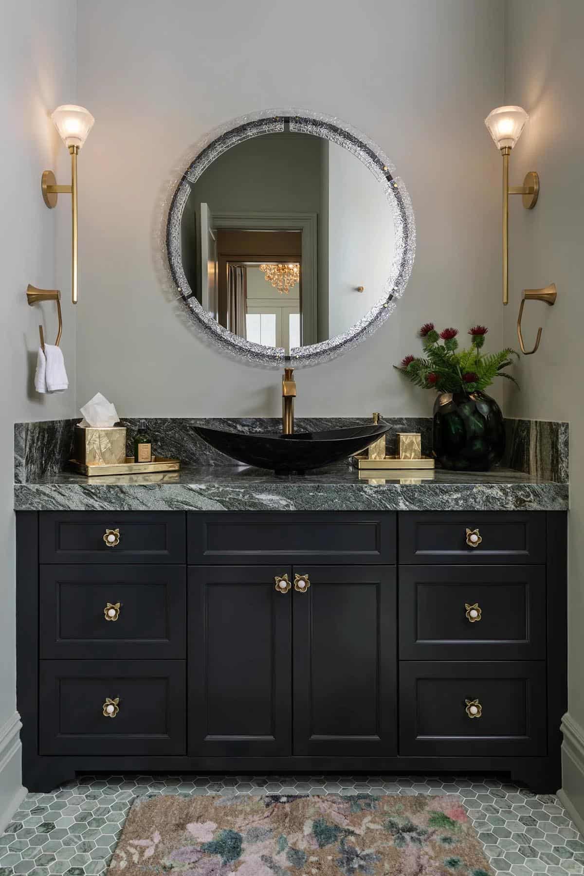 Guest bathroom with black vanity, green marble countertop, crystal-rimmed round mirror, and gold sconces