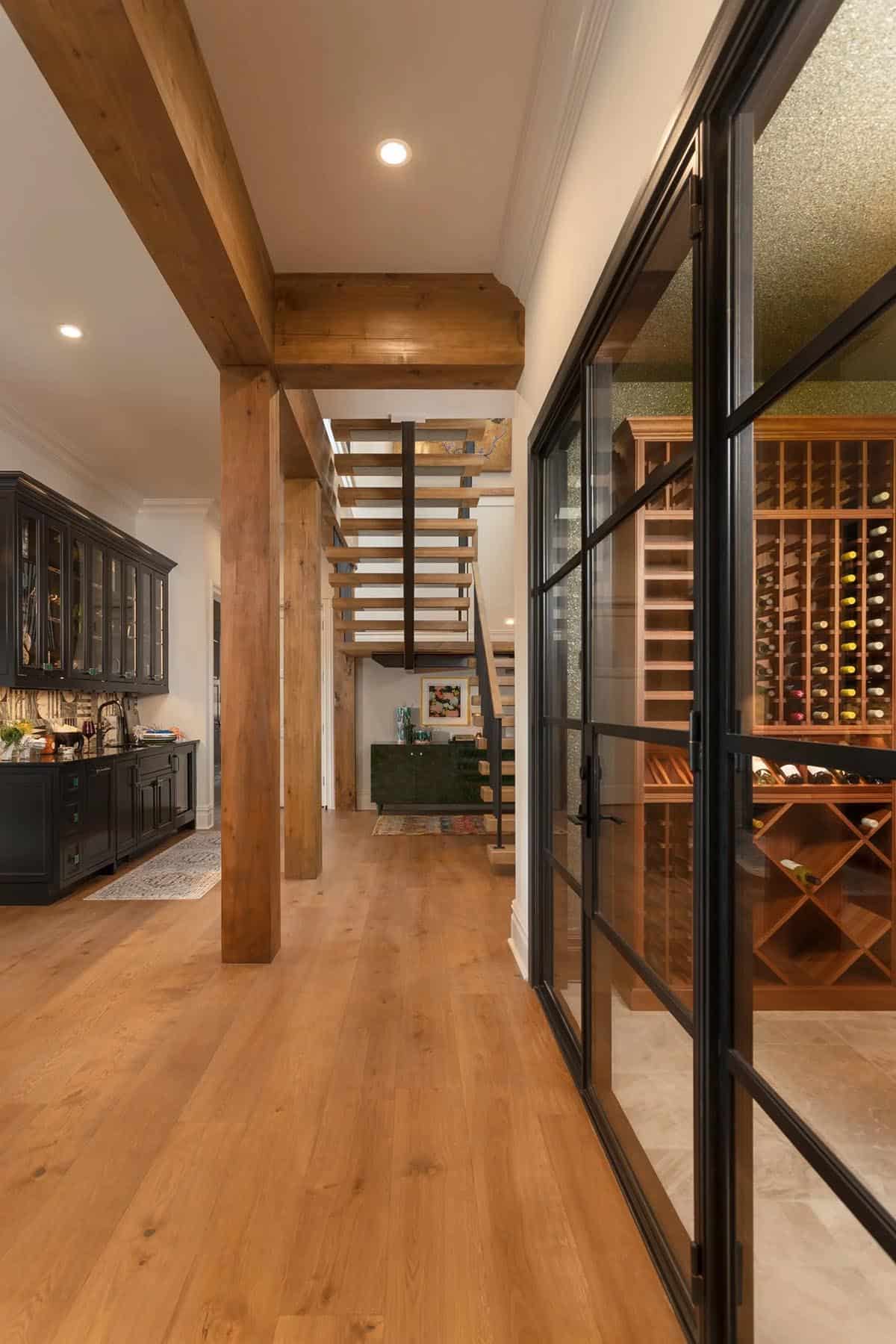 Lower level hallway with glass-walled wine cellar, open-riser oak staircase, and wood beam columns