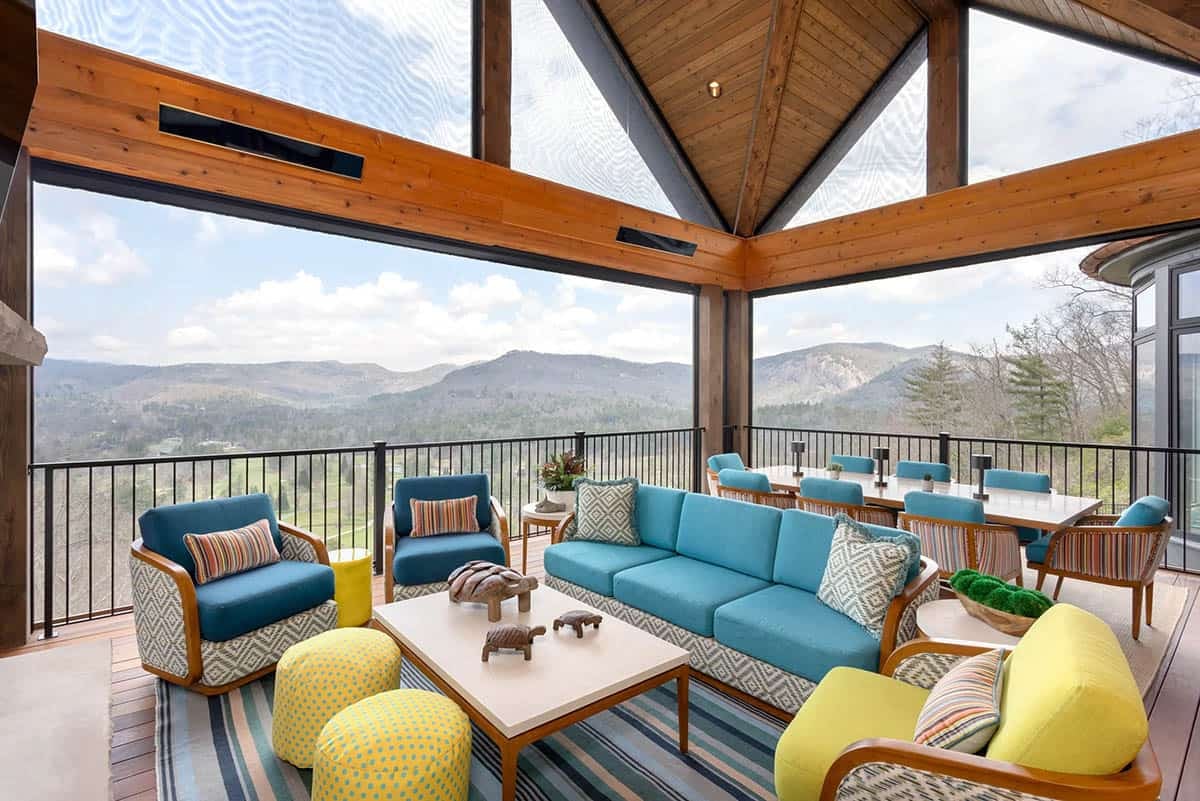 Screened porch with vaulted wood ceiling, teal and yellow outdoor furniture, and panoramic mountain views