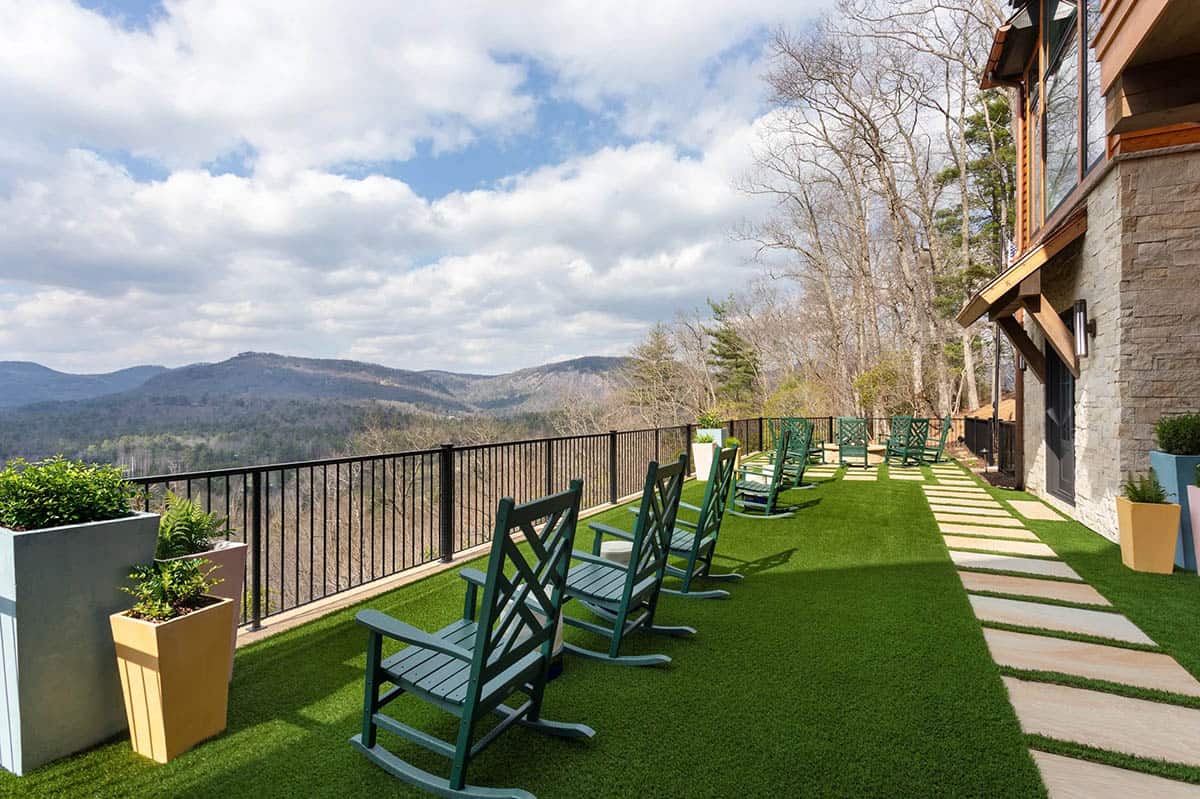 Long terrace with green rocking chairs, turf lawn, stepping stone path, and sweeping mountain views
