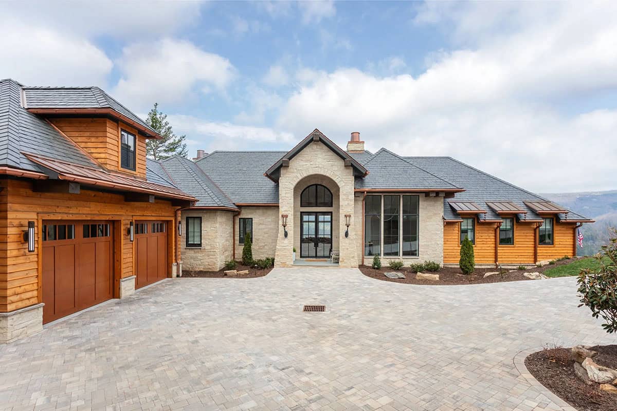 Mountain home front facade with arched stone entry, cedar siding, copper accents, and paver driveway