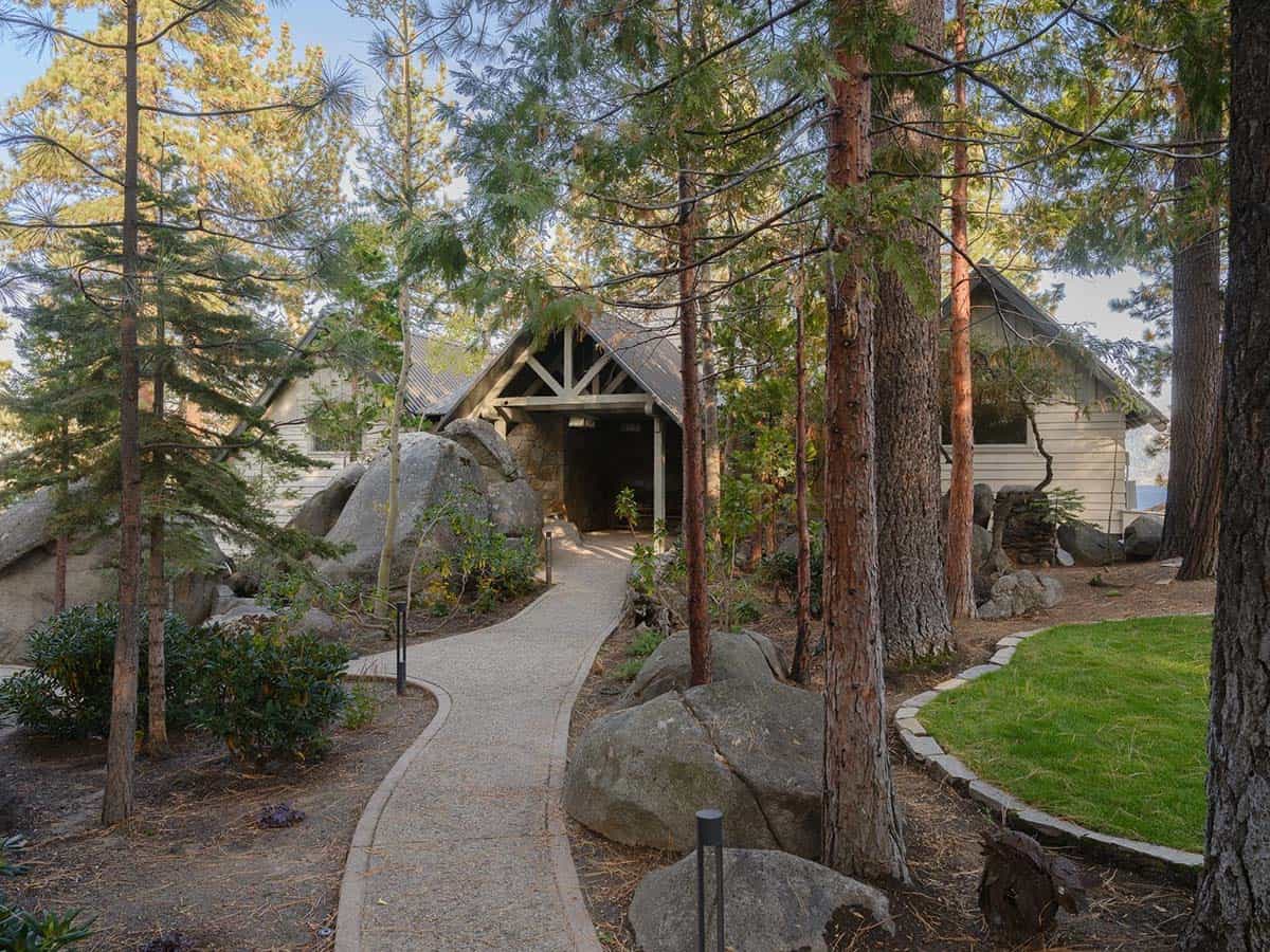 Mountain lodge home exterior with stone entry, timber gable and winding path through pine trees