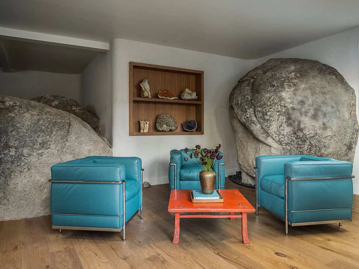 Three teal Le Corbusier chairs and orange coffee table surrounded by granite boulders indoors