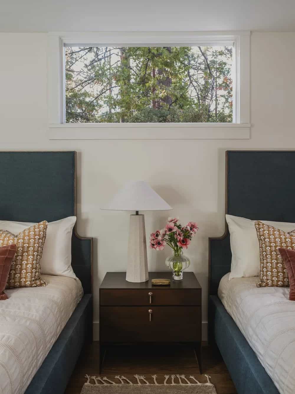 Twin bedroom with dark teal upholstered beds, forest view window and shared nightstand