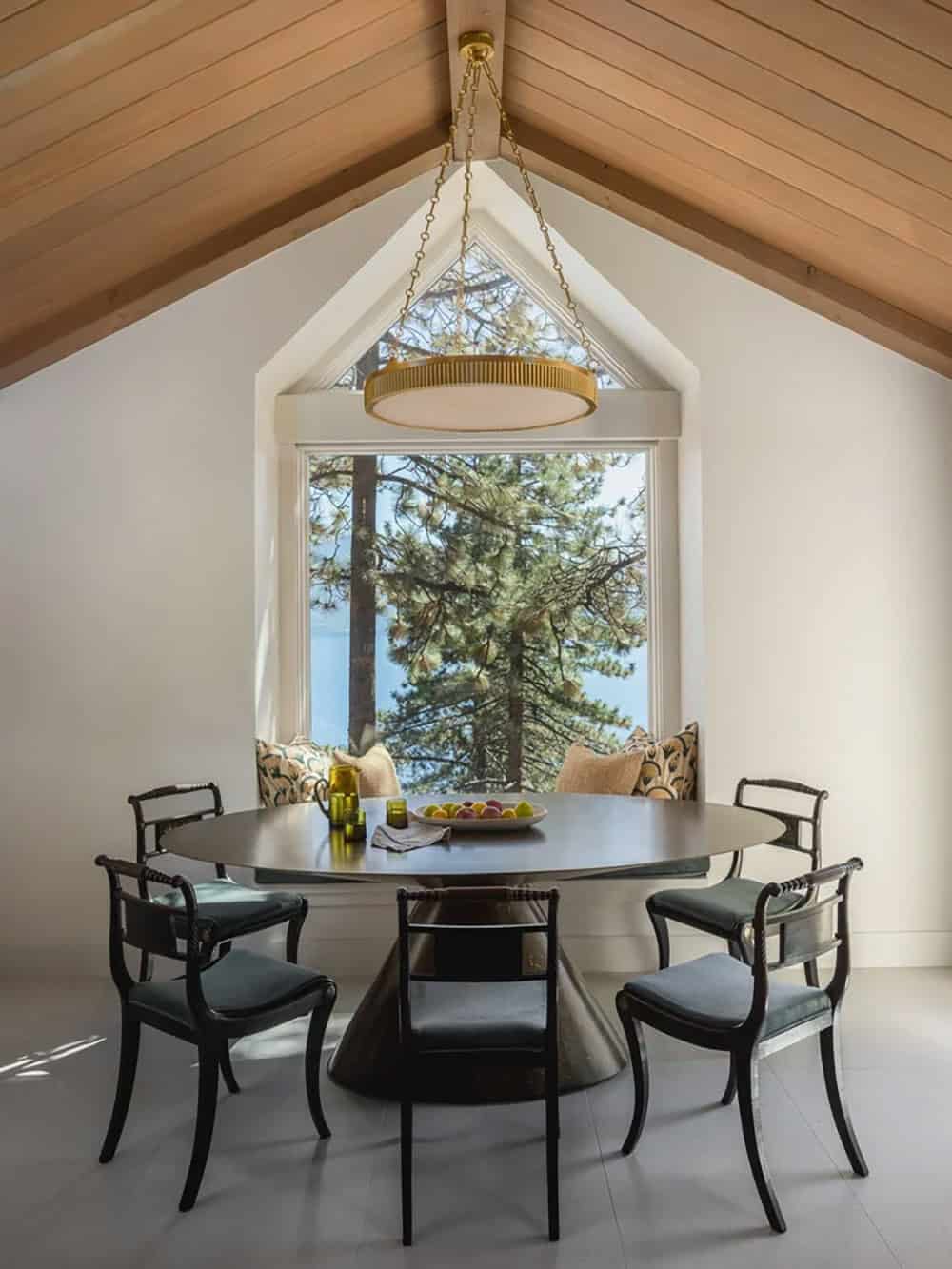 Dining room with round black pedestal table, vaulted ceiling and lake view window seat
