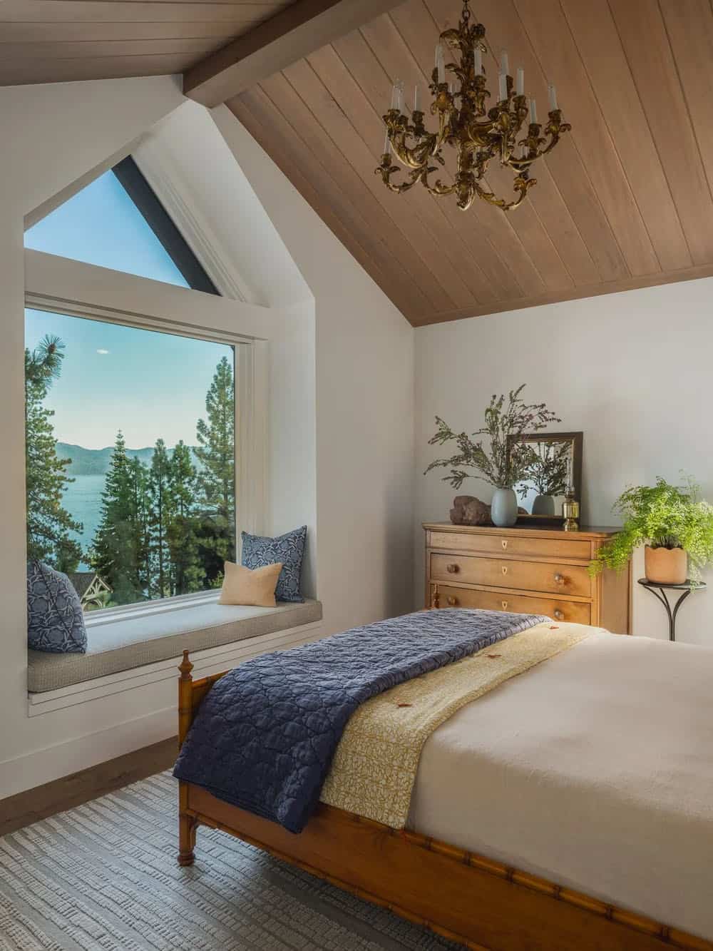 Bedroom with lake view window seat, vaulted ceiling, brass chandelier and antique dresser