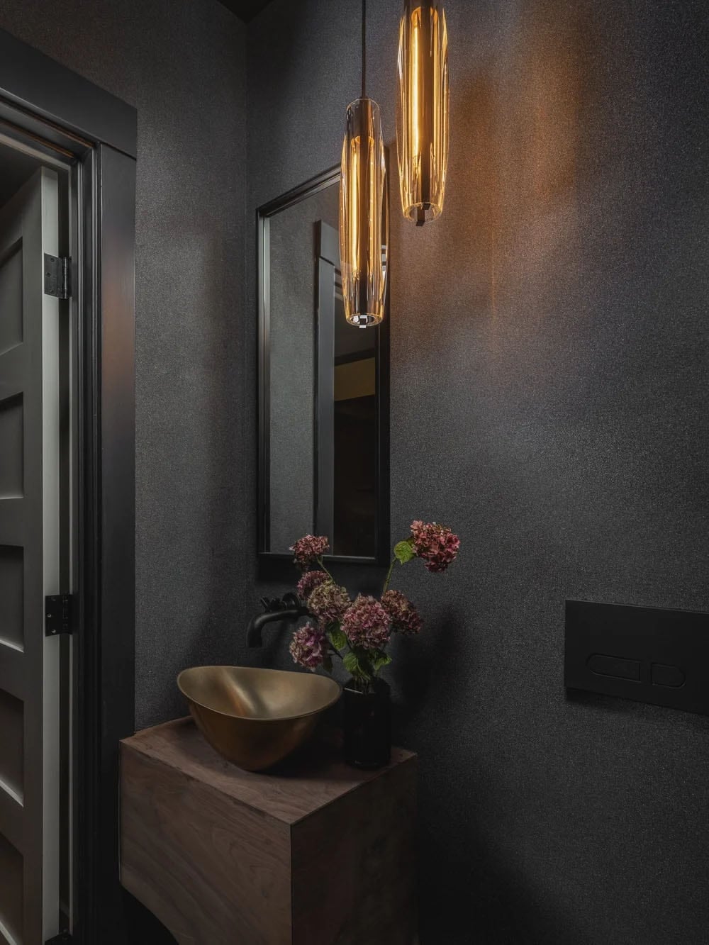 Dramatic powder room with dark textured walls, brass vessel sink and amber glass pendants