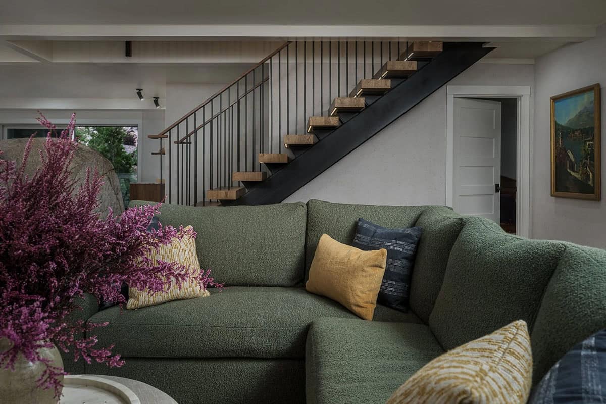 Lower level sitting area with green boucle sofa and floating oak staircase with steel railing