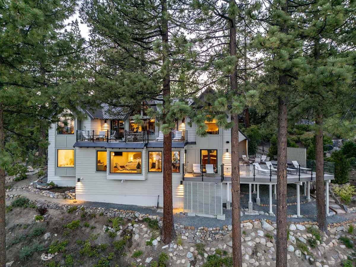 Aerial twilight view of mountain lodge with lit decks and terraces among pine trees