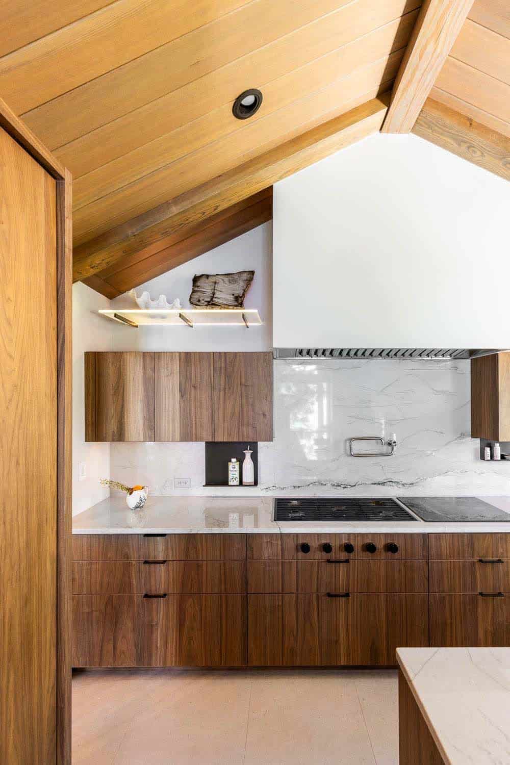 Kitchen cooking wall with walnut cabinetry, marble slab backsplash, white plaster range hood, and induction cooktop