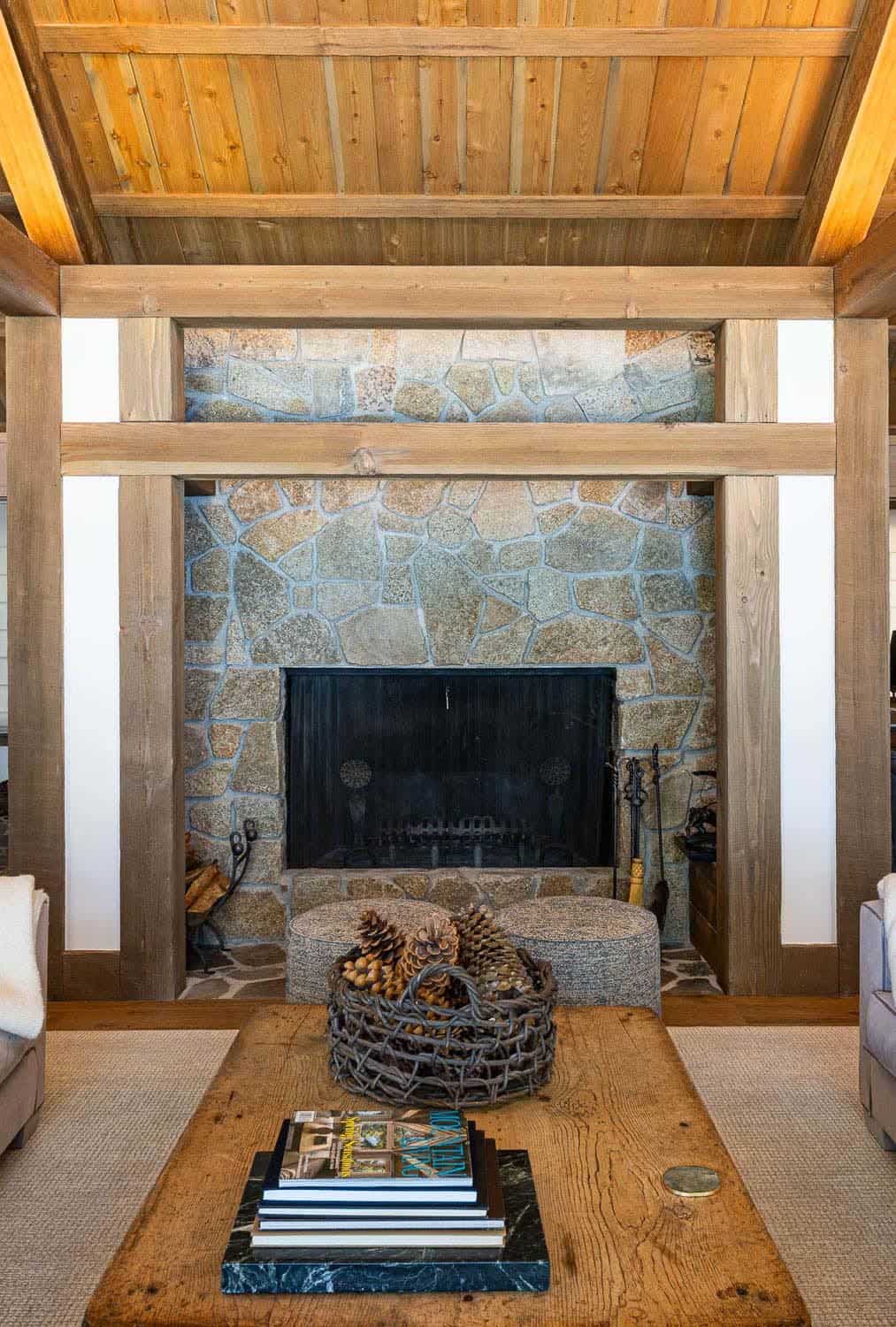 Stone fireplace framed by timber posts with pinecone basket and coffee table books in rustic lodge living room