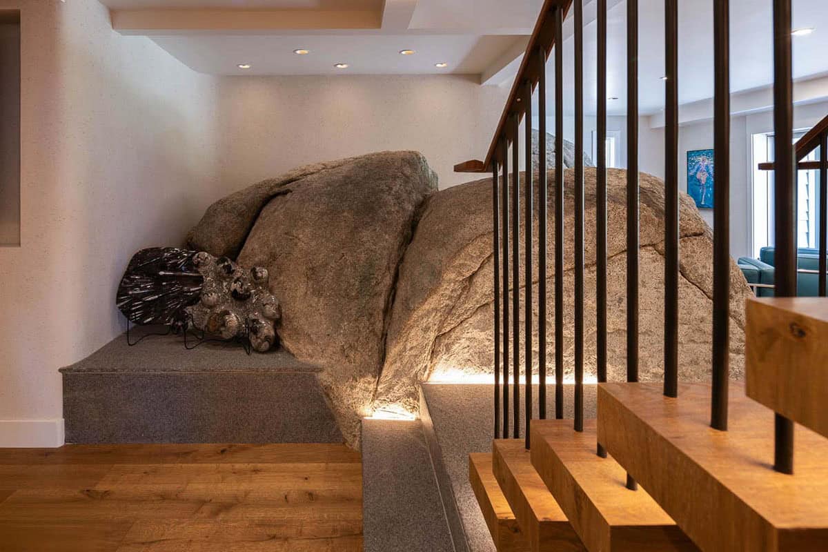 Large granite boulder incorporated into interior staircase landing, dramatically lit from below with warm uplighting