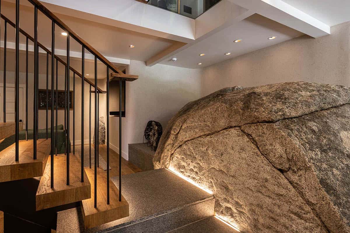 Granite boulders built into lower-level interior, with floating oak staircase and black steel railing alongside
