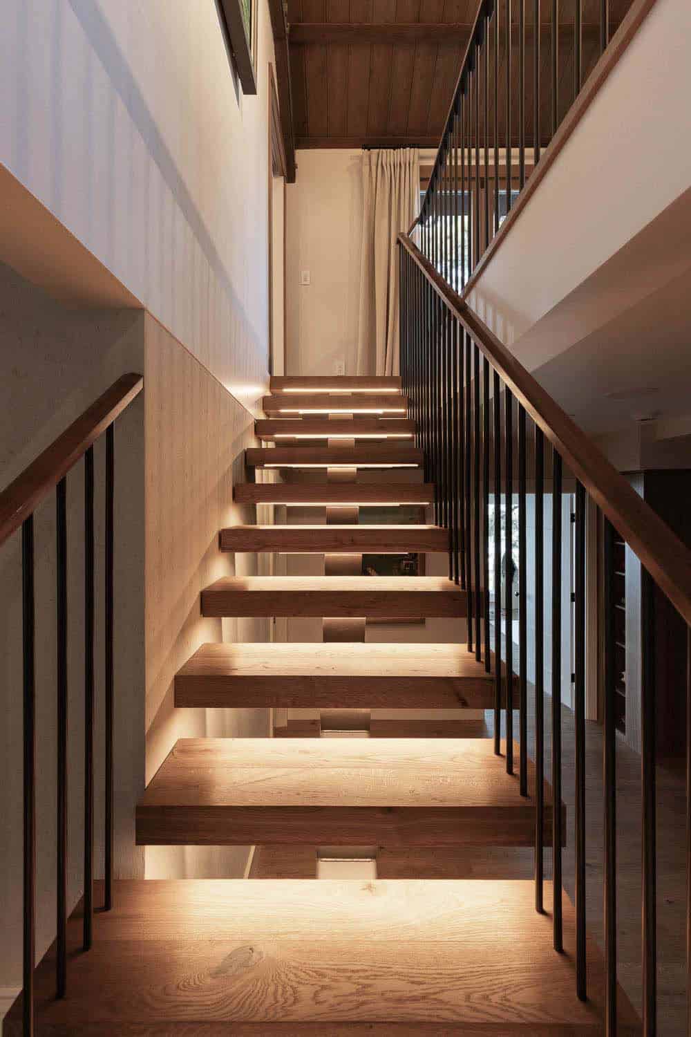 Floating oak staircase with LED step lighting, black steel balusters, and wood handrail in mountain lodge home