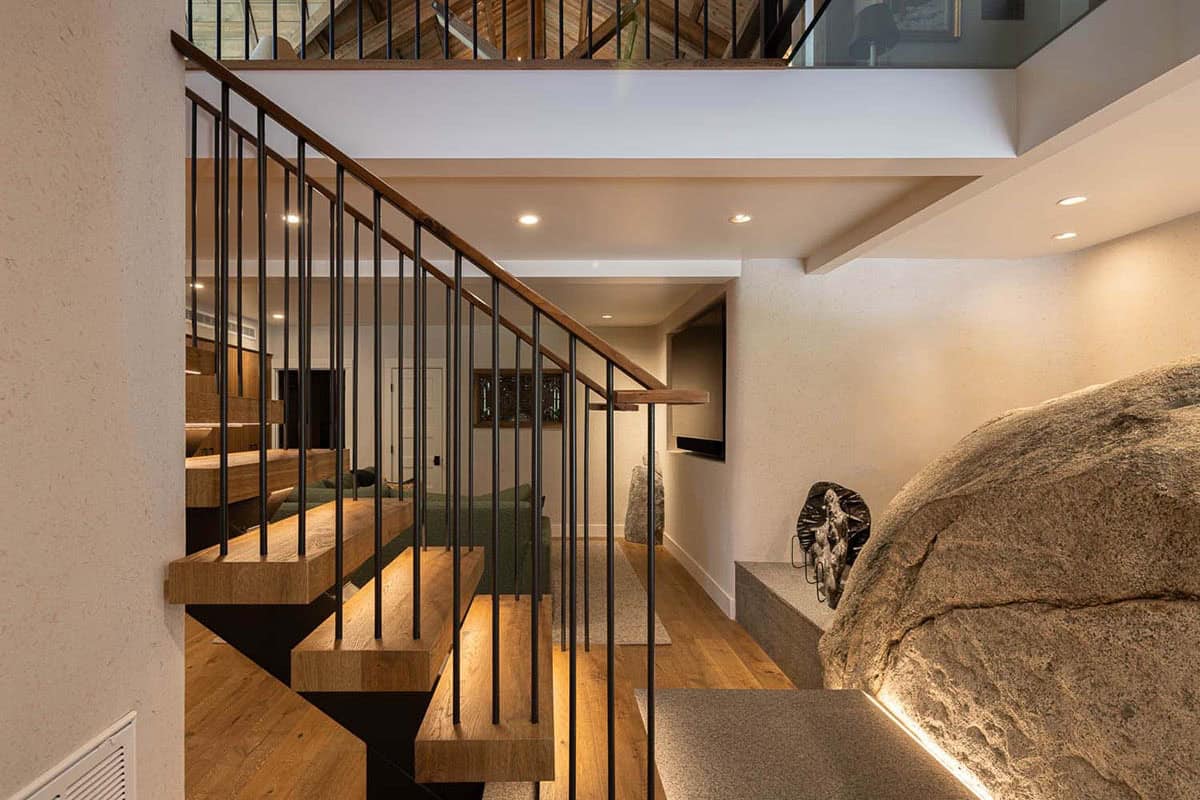 Multi-level interior view of floating staircase, granite boulders, and lower-level living area in Lake Tahoe lodge