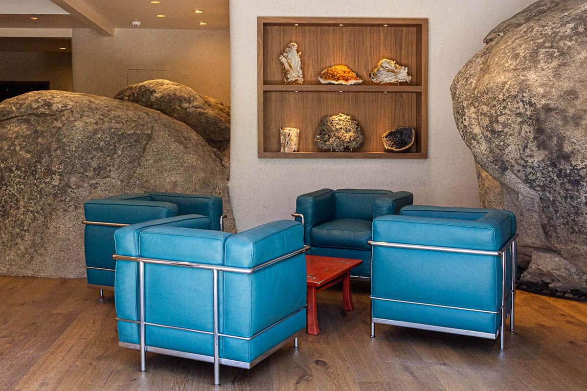 Lower-level lounge with massive granite boulders, teal leather Le Corbusier chairs, and walnut mineral display niche