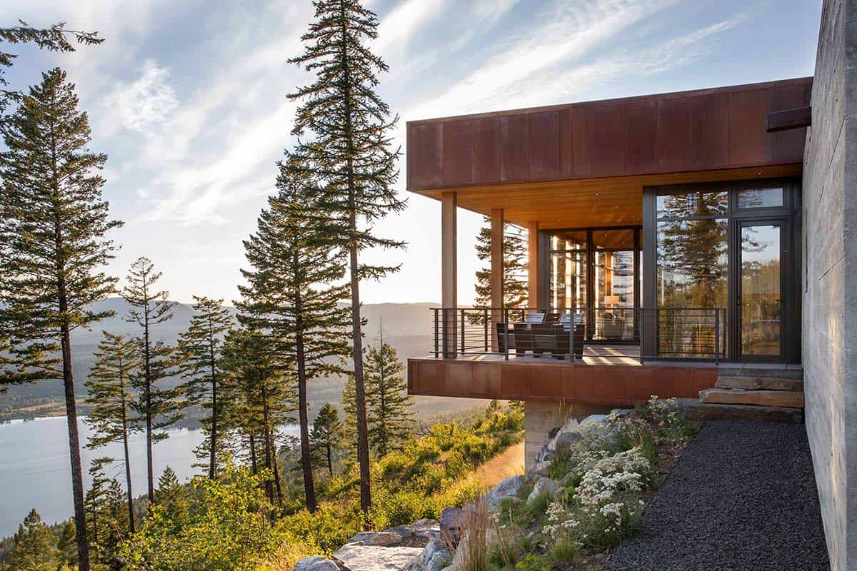 Rust-patina steel exterior and covered balcony with mountain lake views through pine trees