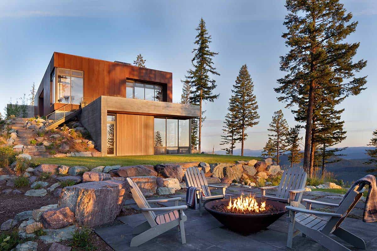 Two-story mountain modern home with fire pit patio and rocky hillside landscaping at dusk