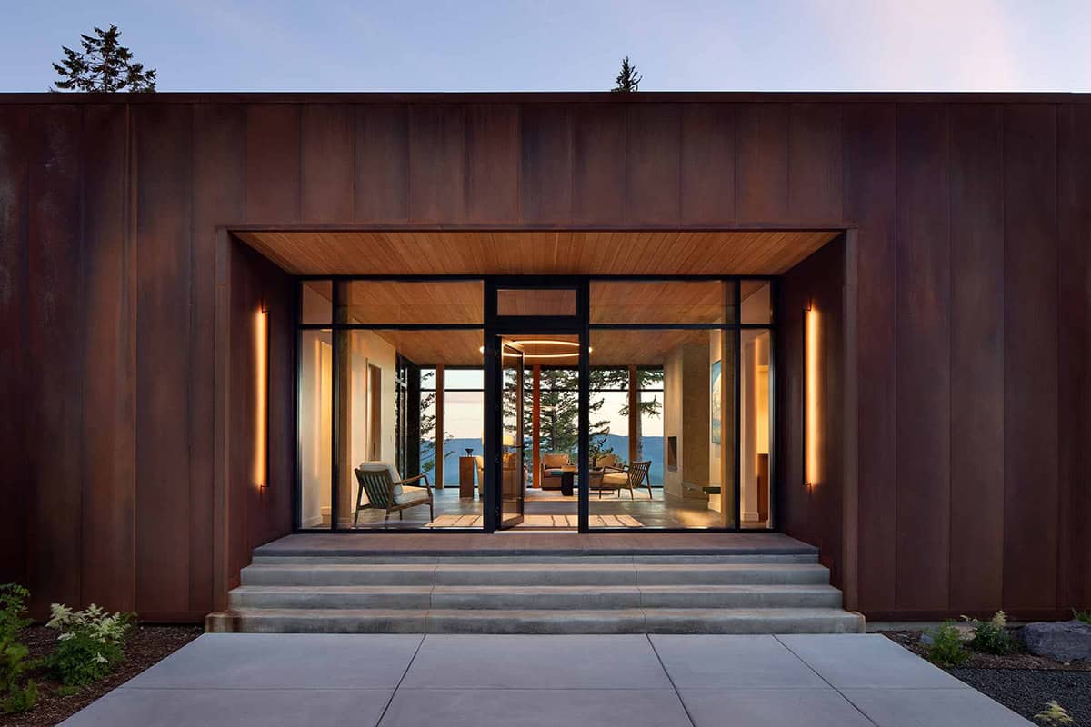 Glass entry doors framed by weathered steel panels with warm interior lighting at dusk