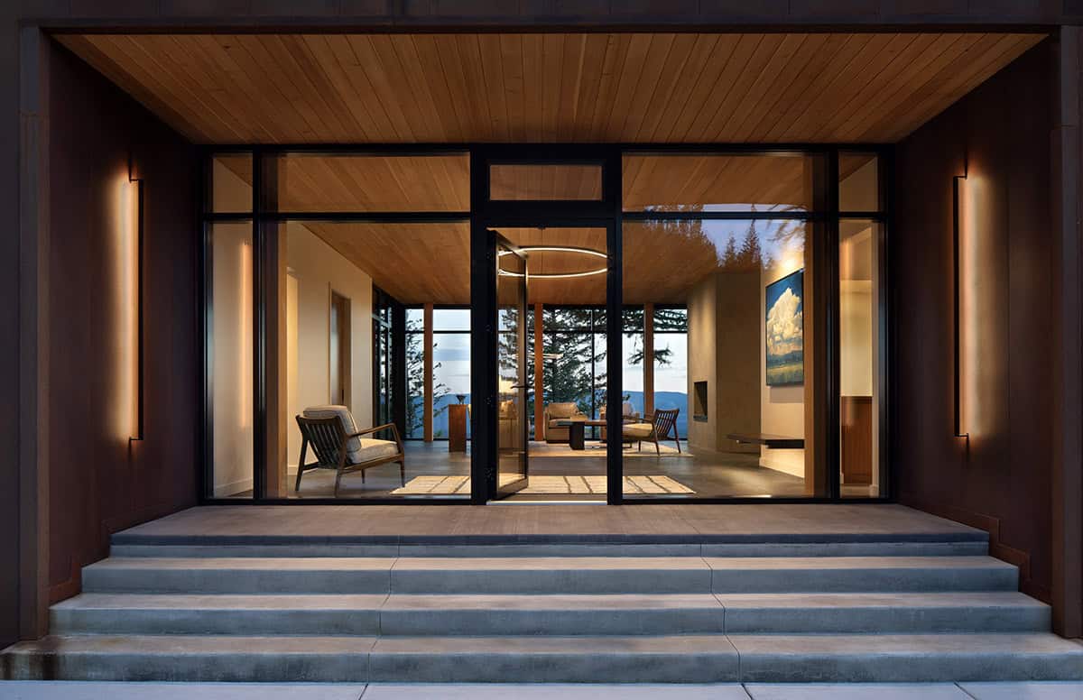 Illuminated entryway with cedar ceiling, steel-framed glass walls, and mountain views beyond
