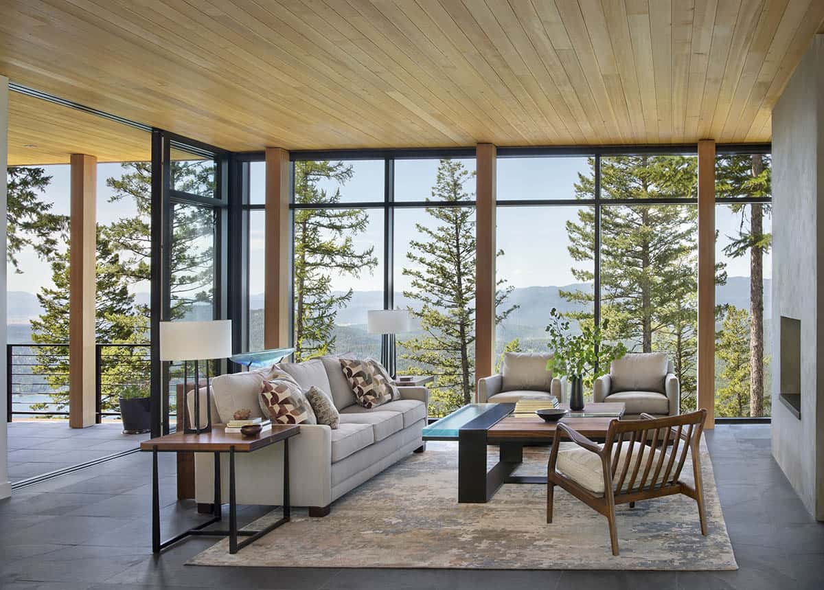 Corner living room with wraparound floor-to-ceiling windows framing pine trees and mountain valley