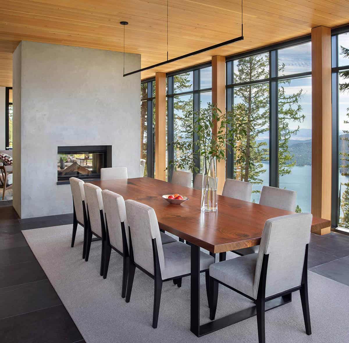 Walnut dining table for ten beside a double-sided fireplace with lake views through glass walls