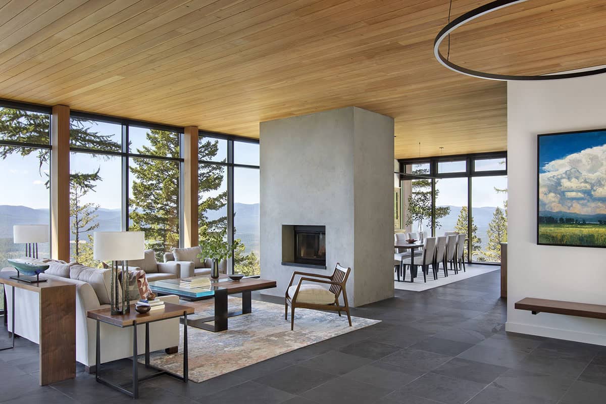 Great room with concrete fireplace dividing living and dining areas under a cedar plank ceiling