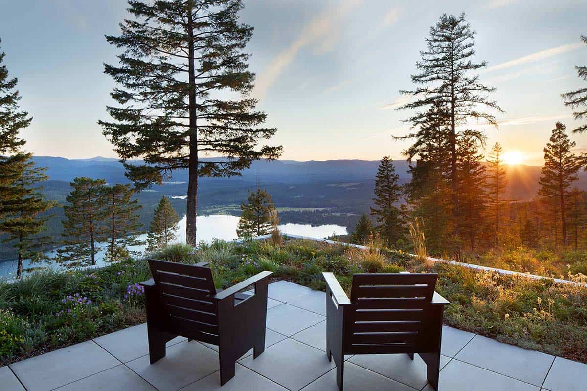 Two modern Adirondack chairs on stone terrace overlooking lake and mountain sunset panorama