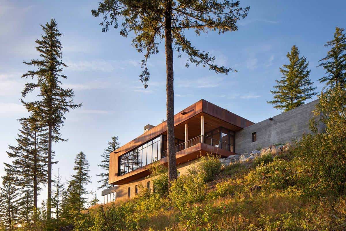 Corten steel clad home rising above forested hillside with large glazed living pavilion