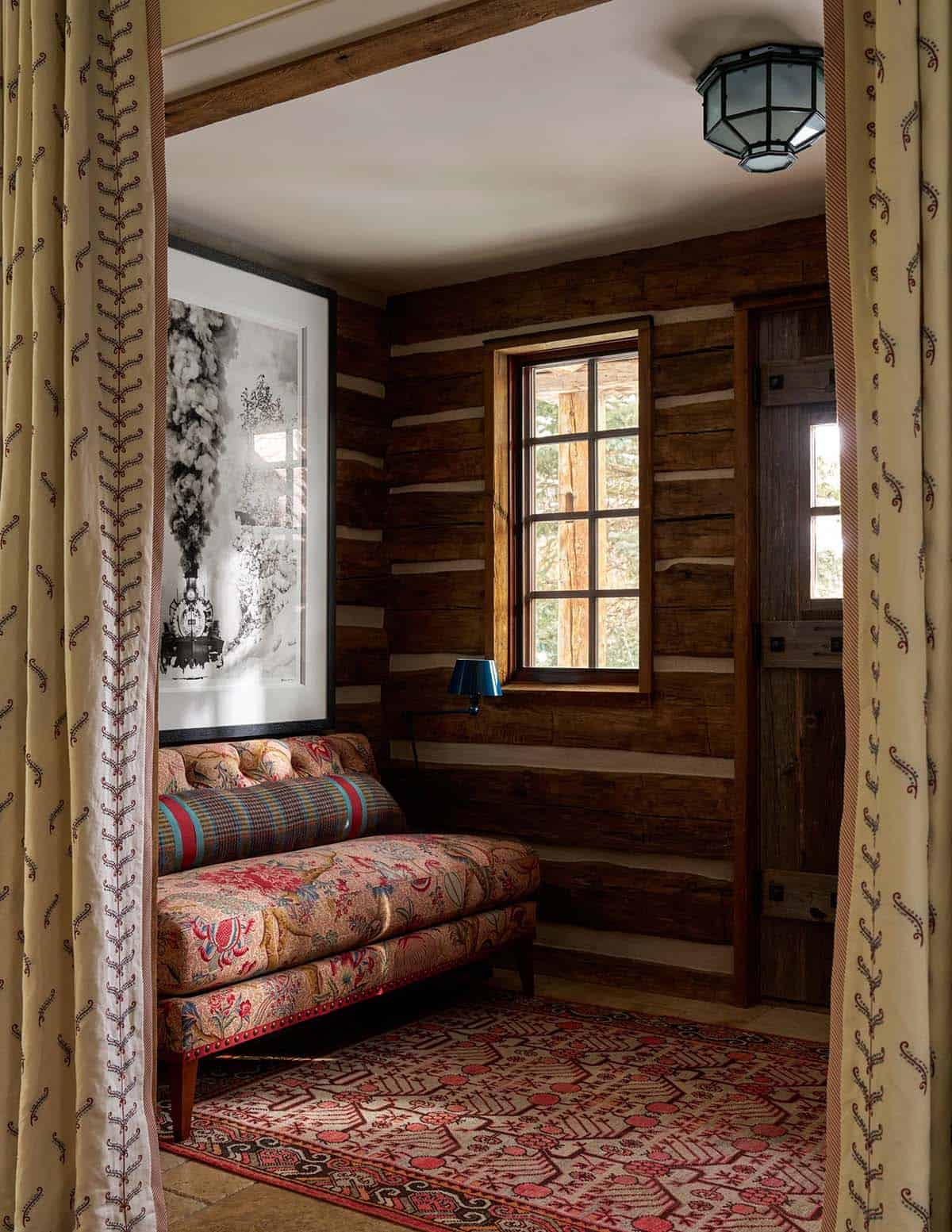 Richly patterned daybed in log cabin nook with Persian rug, printed curtains, and black-and-white artwork