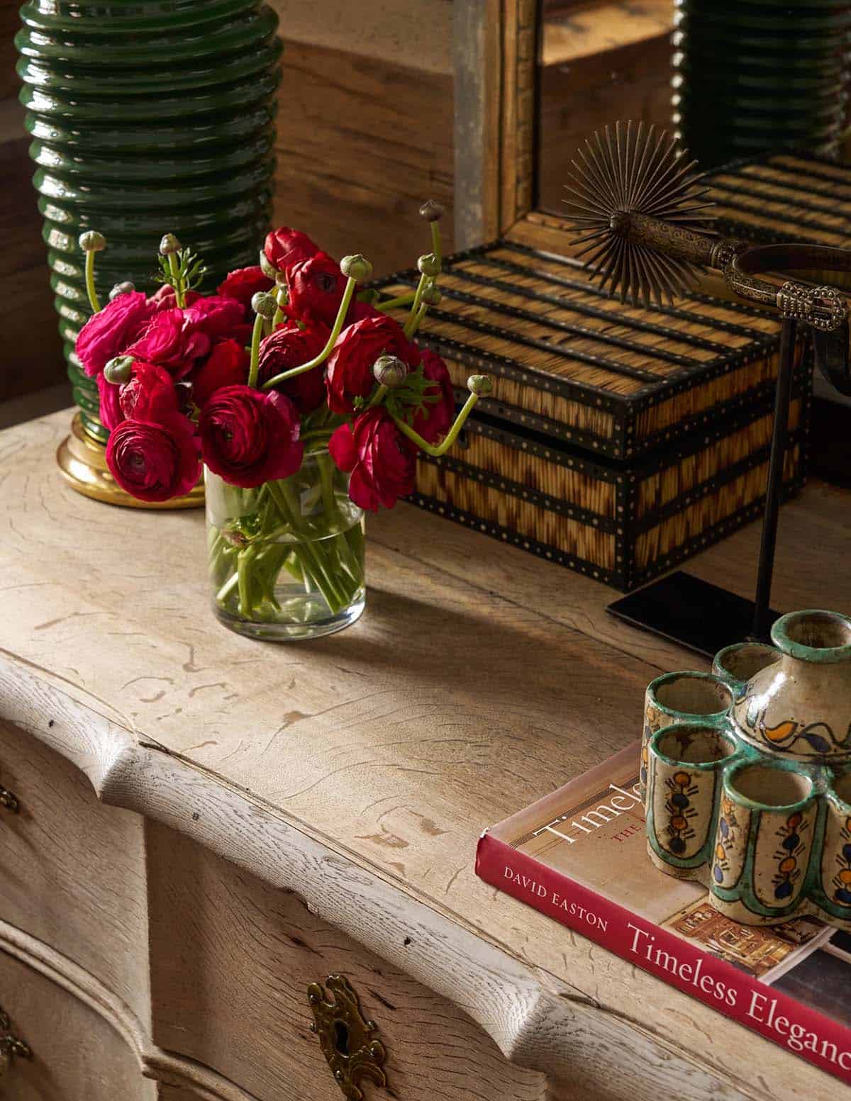 Close-up vignette of antique chest with red ranunculus, decorative box, and David Easton coffee table book