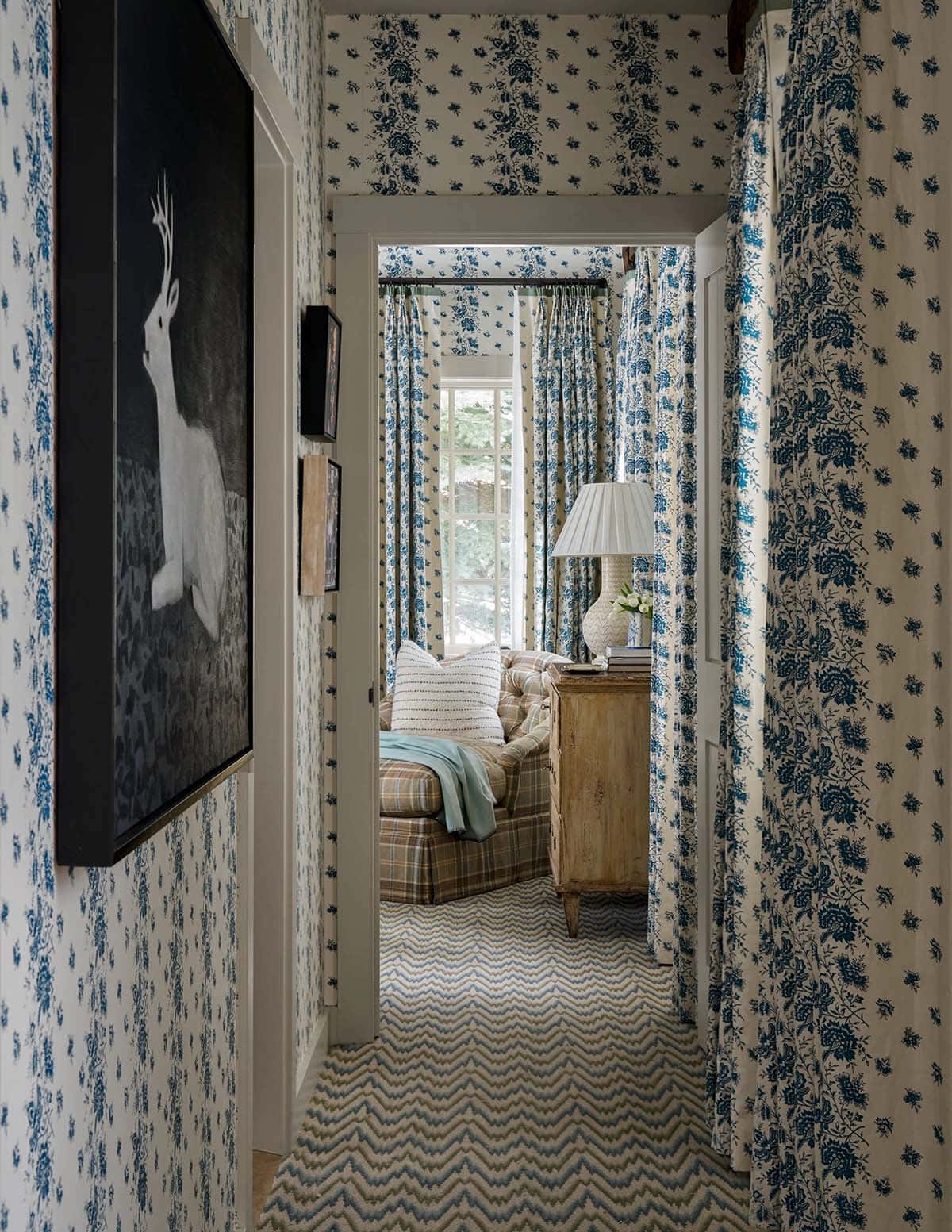 Blue floral wallpapered hallway with chevron carpet leading to plaid guest bedroom with coordinating curtains