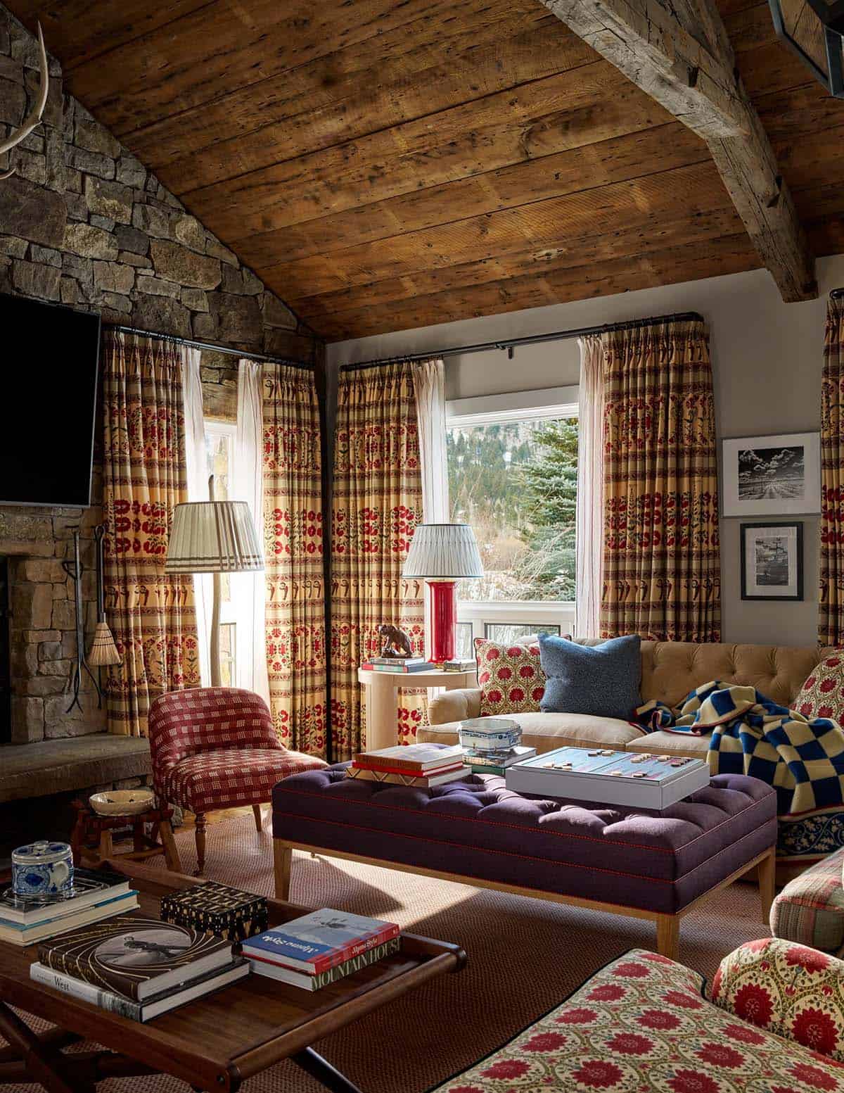 Family room seating area with stone fireplace, tufted purple ottoman, plaid armchairs, and patterned curtains